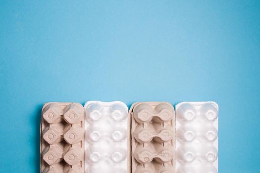 several foam and cardboard packaging for eggs lie in a row on a blue background, top view, copy space, sorting waste concept, environmental materials against plastic