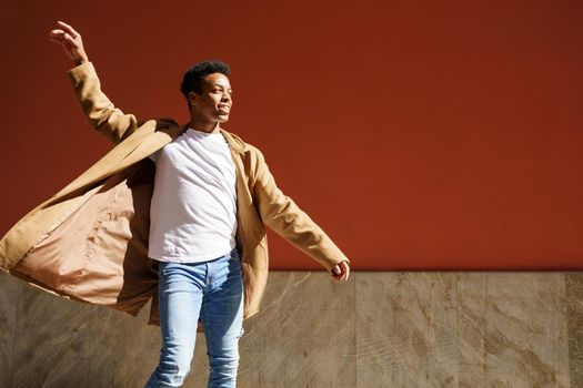 Young black man dancing on red urban wall.