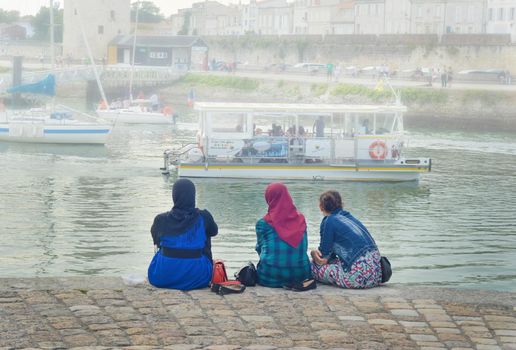 LA ROCHELLE, FRANCE - AUGUST 12, 2015: Muslim woman wearing hijab looking on the ocean and yachts at La Rochelle, France.