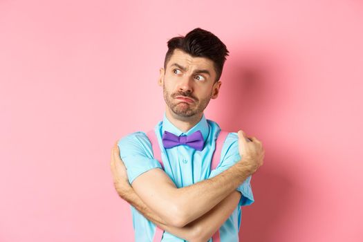 Timid guy feeling offended and lonely, embracing body, comforting himself and looking left upset, standing on pink background