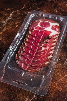 Italian sliced cured coppa meat in vacuum packaging. Dark background. Top view