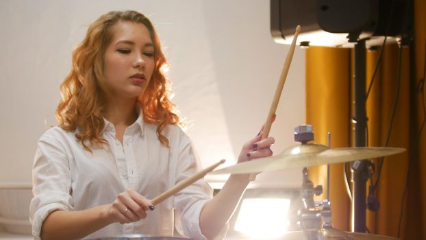 Pretty redhead girl playing drums in studio
