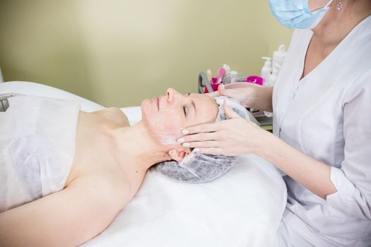 Cosmetologist prepares the client's face for cosmetic procedure of mesotherapy with cream