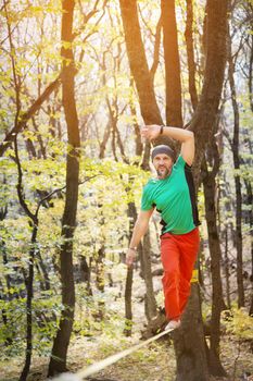 Male tightrope walker balancing barefoot on slackline in autumn forest. The concept of outdoor sports and active life of people aged.