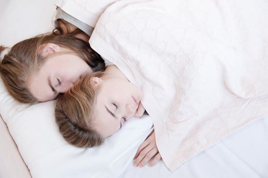 Close-up of a young couple in bed sleeping in an embrace, hiding behind a blanket. The concept of a young family and healthy sleep