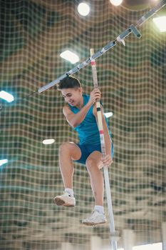 Pole vaulting indoors - young fit smiling man jumping leaning on the pole