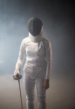 A young woman fencer in protective helmet standing with a sword down