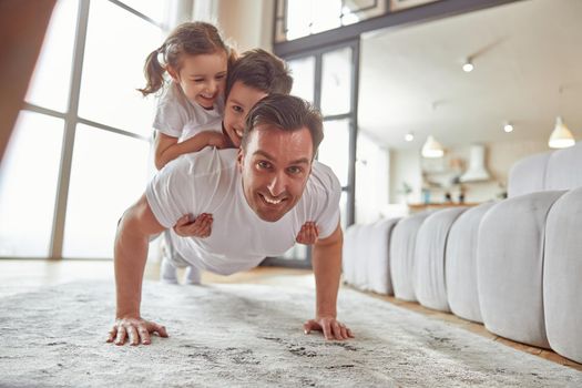 Happy man doing push ups with children at home