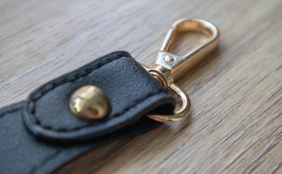 Swivel carabiner fastener with leather black bag strap on a wooden background. Metal carabiner with swivel clip or hook. Small gold fittings close-up in selective focus.