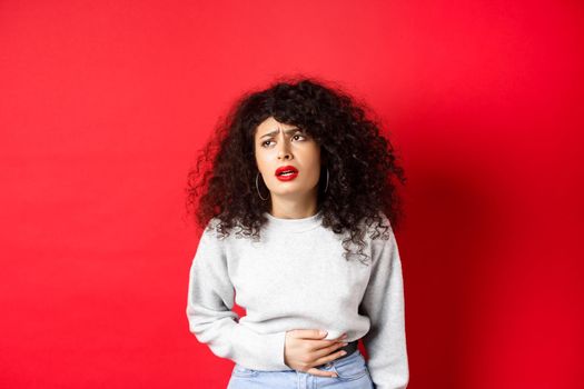 Woman feeling sick, bending and touching belly, having stomach ache or menstrual cramps, standing on red background