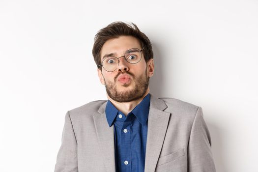 Startled guy in glasses and suit, tilt back and looking shocked or scared at camera, standing against white background