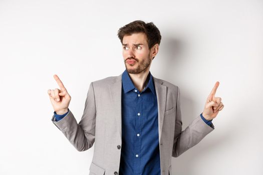 Complicated businessman pointing two ways, troubled to choose, looking aside and thinking, making decision, standing on white background in suit