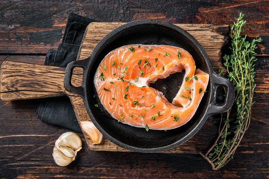Trout or Salmon raw steaks in a pan with thyme. Dark wooden background. Top view