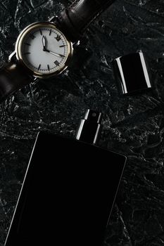 Men's watches and an open bottle of black eau de toilette lie on a dark textured background. Fragrance for men.
