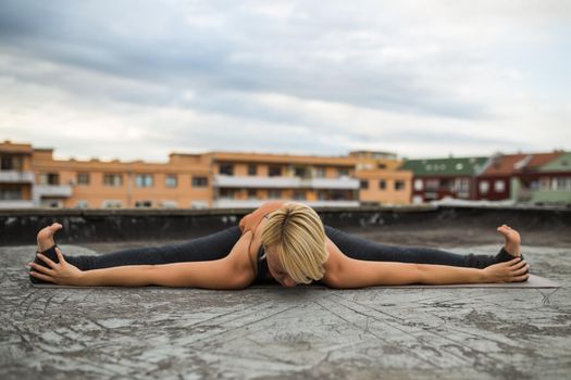 Woman enjoys  practicing yoga on the roof, Upavista konasana.