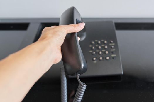 Telephone in a hotel room, hand with a raised telephone receiver close-up