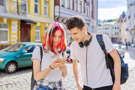 Handsome teenagers couple guy and girl together on city street looking in smartphone screen