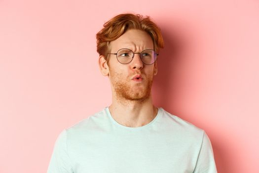 Ouch thats bad. Face of redhead man showing pity and feeling sorry for someone, frowning and looking with compassion, standing over pink background