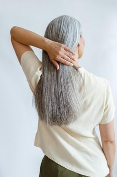 Middle aged woman adjusts long loose hoary hair on light grey background