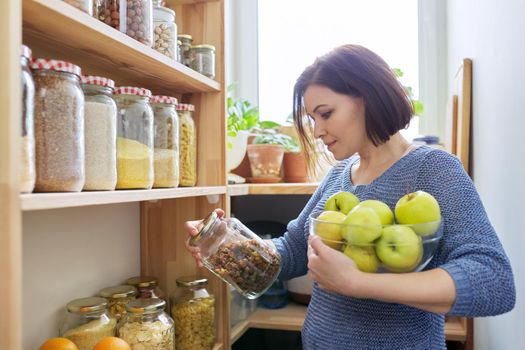 Woman with bowl of green apples in pantry, organizing in kitchen