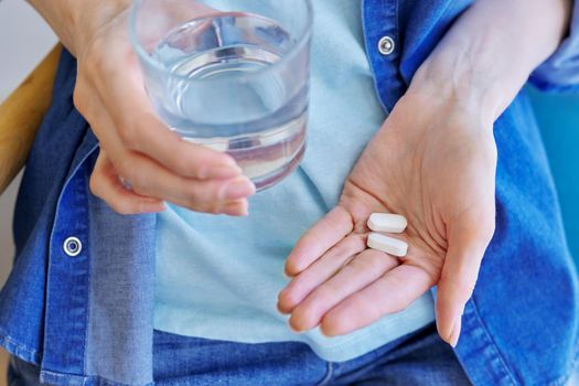 Close-up of mature woman's hand with pills and glass of water