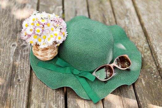 daisies lying on a green hat near sunglasses. Designer old-fashioned floristics bouquet of meadow and wild flowers. A romantic photo of a cute spring bouquet. hat with bouquet of daisies
