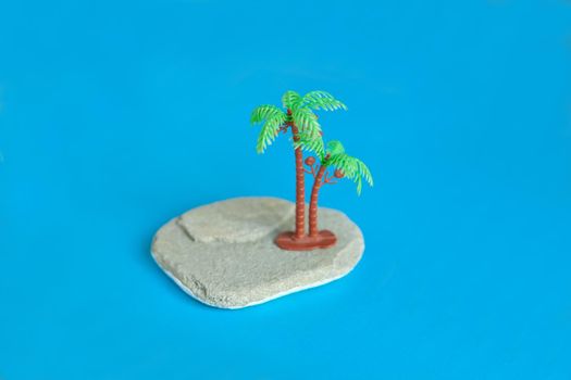 Minimalistic image plastic toys at the beach - toy palmtree on the stone at blue paper.
