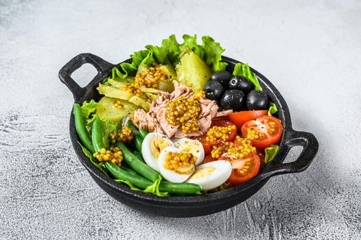 Gourmet nicoise salad with vegetables, eggs, tuna and anchovies in a pan. White background. top view