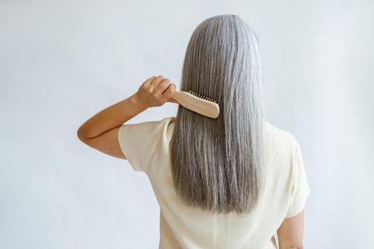 Lady brushes straight silver hair standing on light grey background