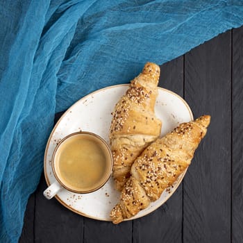 Fresh croissants and cup of coffee on black table. Copy space, top view