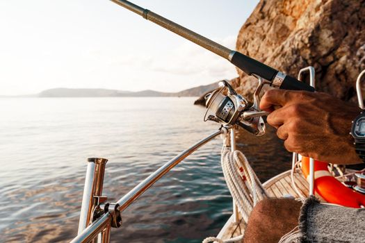 Close up of male hands holding fishing rod while fishing on sailboat in open sea