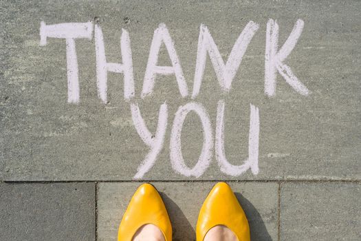 Female feet with text thank you written on grey sidewalk