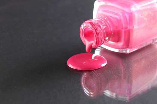 Pink nail polish is poured out of the bottle bottle on a black background with a copyspace place for text