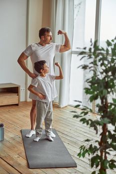 Sporty father and son demonstrating muscles indoors