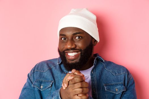 Close-up of devious and happy african-american man smiling satisfied, clasp hands think something good, expect profit, standing over pink background
