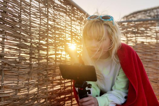 Outdoor sunset portrait of female teenager recording video on smartphone
