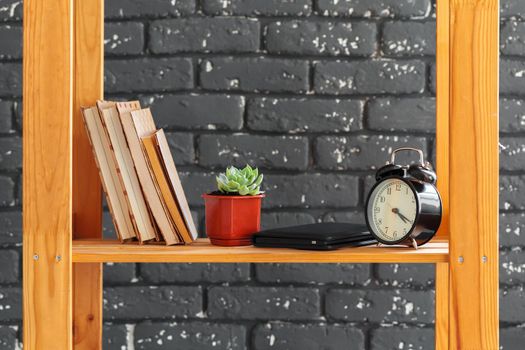 Wooden bookshelf with books and stuff against black brick wall
