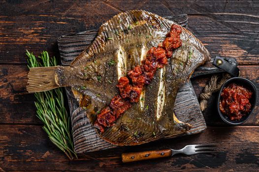 Grilled Flounder or plaice with tomato sauce on wooden cutting board. Dark wooden background. Top view