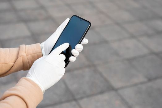 Young woman holding a mobile phone in her hands wearing latex protective gloves