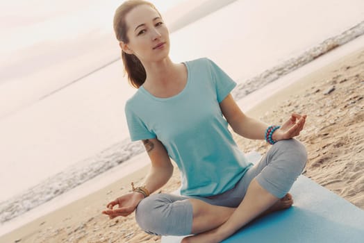 Woman meditating in lotus position on shore.