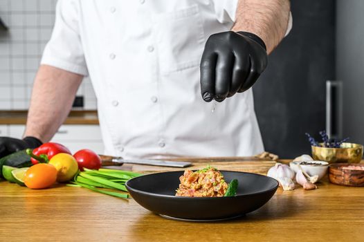 The chef in black gloves prepares tartare from fresh tuna fish
