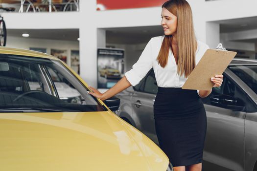Attractive young female car dealer standing in showroom