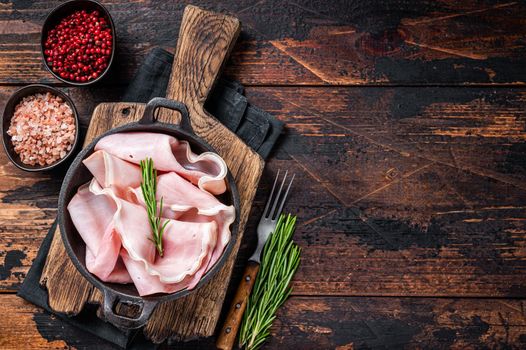 Prosciutto ham sliced in a pan. Dark wooden background. Top view. Copy space