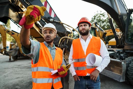 Two men engineers discussing their work standing against construction machines