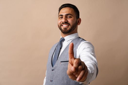 Young arabian businessman pointing finger to camera against beige background
