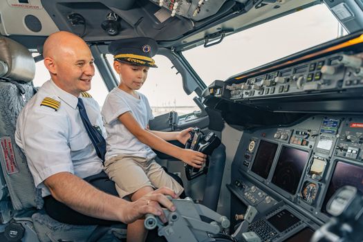 Smiling mature pilot and kid sitting in cabin