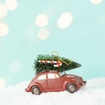 Red toy car with christmas tree aginst blue background with christmas lights