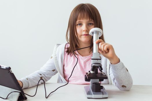 Schoolgirl using microscope in science class. Technologies, lessons and children concept.