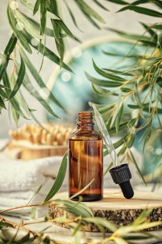 Amber glass bottle with wooden massage brush, eucalyptus leaves, mirror and towels. Eco friendly massage and body care concept