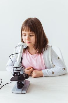 Schoolgirl using microscope in science class. Technologies, lessons and children concept.